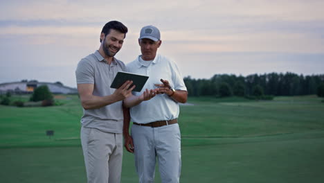 Two-golfers-search-tablet-on-field-landscape.-Happy-men-chatting-online-outside.