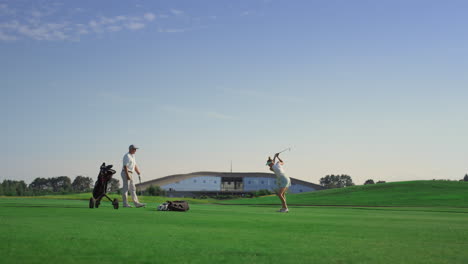 Two-golf-players-training-at-course-field.-Couple-playing-sport-game-in-sunset.