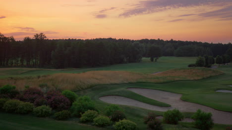 Golf-course-aerial-view-in-evening-pink-sunset.-Empty-fairway-green-grass-field.