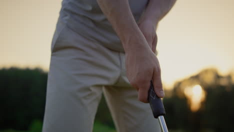 Professional-golf-player-hands-holding-club-putter-on-sunset-fairway-field.