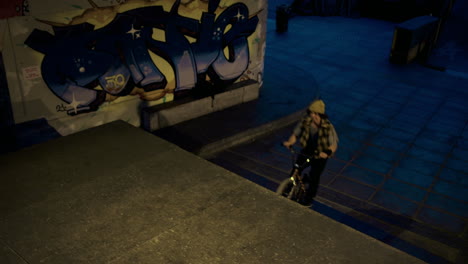 Active-man-jumping-bmx-bicycle-through-steps-at-skate-park-with-graffiti-wall.