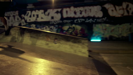 Young-people-jumping-on-ramp-at-night-skate-park-with-graffiti-wall.