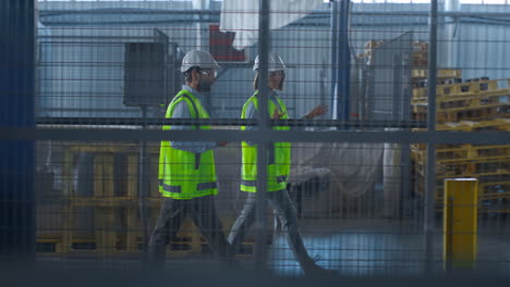 Two-uniformed-warehouse-workers-discussing-manufacture-production-inspecting