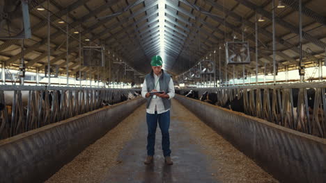 Livestock-supervisor-holding-tablet-computer-in-modern-cowshed-farm-facility.