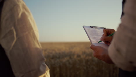 Partners-signing-contract-wheat-field.-Farmers-hands-hold-clipboard-close-up.