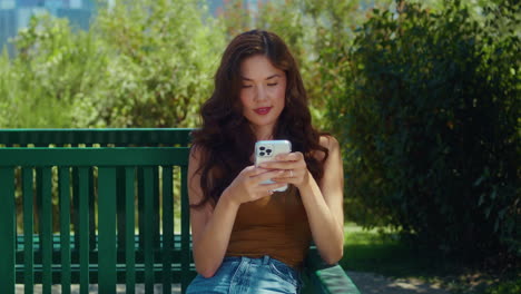 Focused-girl-surfing-internet-on-park-bench-closeup.-Asian-woman-scrolling-phone