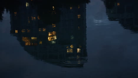Water-reflecting-night-buildings-drone-shot.-Calm-river-lake-ripples-waving.