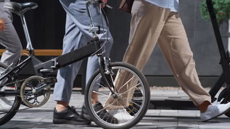 Workers-legs-walking-downtown-with-electric-scooter-bicycle-in-hands-close-up.