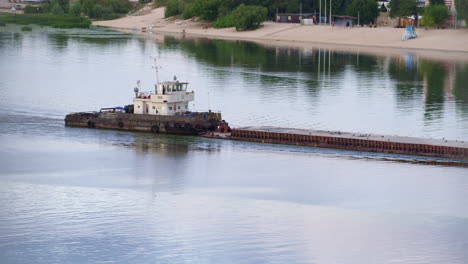 Tug-flowing-along-river-daylight-drone-shot.-Tow-boat-pushing-old-empty-barge.