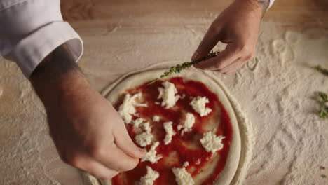 Professional-chef-prepare-pizza-dough-on-table.-Man-cook-adding-herbs-in-kitchen