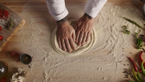 Pastry-cook-hands-kneading-raw-bread-dough-on-restaurant-kitchen-cutting-board.