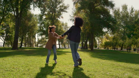 Smiling-mother-playing-together-daughter-dancing-on-green-spring-park-field.