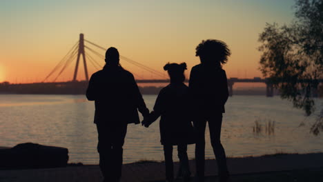 Loving-family-silhouette-walking-to-river-shore-together-at-beautiful-sunset.