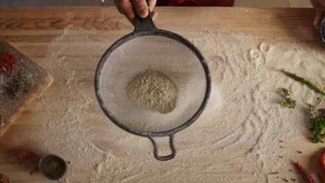 Baker-cooking-sifting-flour-on-wooden-cutting-board-in-pizza-restaurant-kitchen.