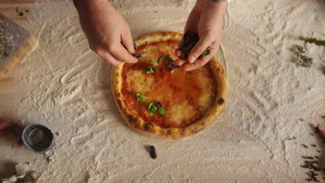 Chef-hands-preparing-recipe-adding-ingredients-on-italian-pizza-at-restaurant.