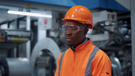 Ingeniero-Afroamericano-Mirando-Cámara-En-Fábrica-Industrial