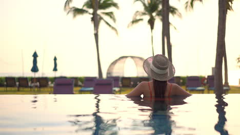 Back-of-Lonely-Young-Woman-in-Infinity-Pool-on-Summer-Evening-at-Exotic-Location-Slow-Motion-Wide-View
