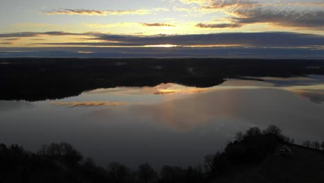 Aerial-Silhouette-of-a-golden-sunset-reflecting-on-lake-surface-at-the-horizon