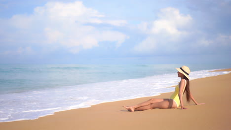 Asian-woman-sitting-on-the-beautiful-clean-sand-beach,-side-to-the-camera,-foamy-sea-tides-slow-motion