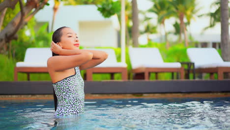 Emerging-from-the-warm-pool-water-at-a-luxurious-resort,-a-young-woman-pushes-the-wet-hair-back-from-her-face