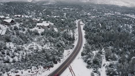 Aerial-view-of-a-solo-red-car-driving-through-Arizona's-snow-covered-rural-forests