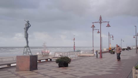 Senior-couple-walking-on-the-promenade-along-the-coastline-of-De-Haan-in-Belgium-during-a-windy-autumn-day