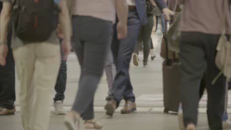 Handheld-shot-of-a-crowd-of-unrecognizable-people-going-back-and-forth-on-a-walkway-in-summer,-mostly-showing-legs-and-shoes