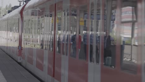 Medium-shot-of-a-red-train-of-the-Deutsche-Bahn-arriving-at-a-station-near-Munich,-Germany,-with-many-busy-people-exiting,-in-a-documentary-style-handheld-shot,-all-objects-in-focus