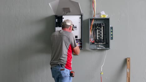 Technician-using-a-drill-to-hang-the-power-system-control-station-on-the-wall-next-to-the-circuit-breaker-box