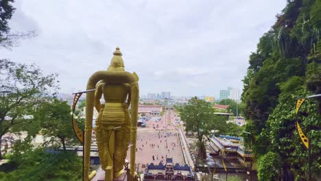 Toma-En-ángulo-Alto-Desde-La-Parte-Superior-De-Las-Escaleras-De-La-Parte-Trasera-De-Una-Estatua-Dorada-Del-Dios-Hindú-Murugan-Frente-Al-Templo-Subramanya-A-Lo-Largo-De-Las-Cuevas-De-Batu,-Malasia