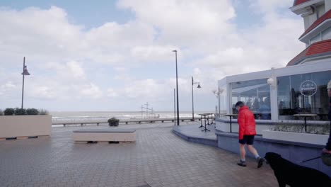 Touristen,-Die-An-Der-Meerpromenade-Mit-Blick-Auf-Die-Nordsee-Im-Hintergrund-Ankommen---De-Haan,-Belgien