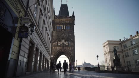 Gente-O-Turistas-Caminando-Bajo-La-Torre-Del-Puente-De-La-Ciudad-Vieja-En-Praga,-Vista-De-Gran-Angular-Bajo,-República-Checa