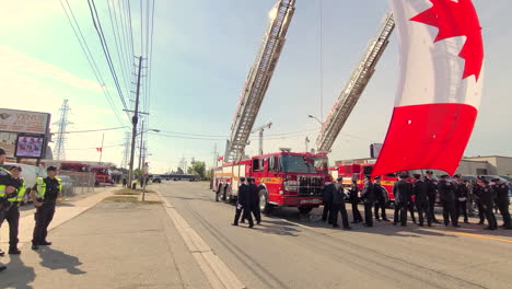 Canadian-fire-department-memorial-ceremony,-Canadian-flag-hanging-on-fire-trucks,-firemen-gathered-on-street