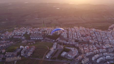 Powered-paraglider-trike-flight-above-Ginosa-in-Italy-at-dusk,-aerial