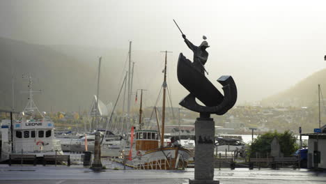 Fangstmonument---Escultura-Con-Tráfico-Y-Puerto-Al-Fondo-En-Tromso,-Noruega