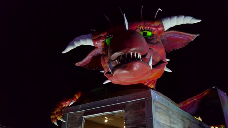 Low-angle-shot-of-an-automated-red-dragon-revolving-it's-head-in-an-amusement-park-in-London,-UK-at-night-time