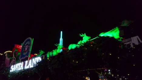 Low-angle-shot-of-Santa-Claus-in-a-sleigh-with-reindeer-inside-an-amusement-park-in-London,-UK-at-night-time