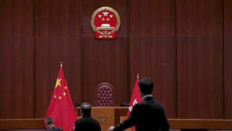 Gesetzgeber-Sind-In-Der-Hauptkammer-Des-Gebäudes-Des-Gesetzgebenden-Rats-Zu-Sehen,-Da-Das-Chinesische-Emblem-über-Der-Flagge-Der-Volksrepublik-China-Im-Hintergrund-Zu-Sehen-Ist