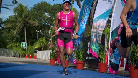 Dos-Jóvenes-Atletas-Masculinos-Vestidos-Con-Un-Traje-Rosa-Y-Azul-Y-Gafas-De-Sol-Corriendo-Hasta-La-Línea-De-Meta-De-Una-Competencia-De-Triatlón