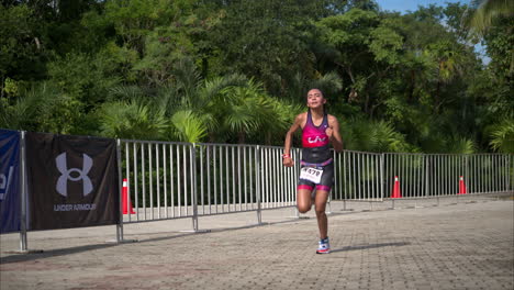 Cámara-Lenta-De-Un-Atleta-Adolescente-Con-Un-Traje-Rosa-Y-Morado-Corriendo-La-Etapa-Final-De-Una-Competencia-De-Triatlón