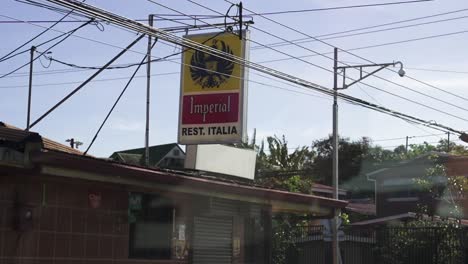 Small-fonda-restaurant-Italia-with-sign-promoting-Imperial-beer-eagle-sign,-Dolly-in-vehicle-shot