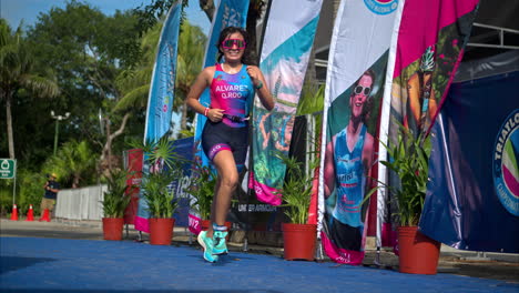 Cámara-Lenta-De-Una-Joven-Atleta-Con-Traje-Corriendo-Hasta-La-Línea-De-Meta-De-Una-Competencia-De-Triatlón-Que-Parece-Exhausta