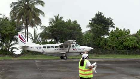 Cessna-208B-Grand-Caravan-EX-single-engine-plane-preparing-to-take-off-from-rural-airport-with-ground-support-crew-woman,-Sansa-Airlines,-Locked-shot