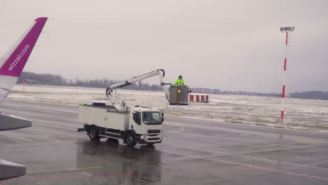 El-Trabajador-Del-Aeropuerto-Está-Rociando-Líquido-Descongelado-En-El-Ala-Plana-En-Un-Día-Nublado-Y-Nevado-Antes-Del-Vuelo-En-Invierno