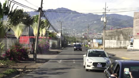 Coches-Conduciendo-En-Una-Calle-De-Sentido-único-Con-Montañas-Detrás,-Cámara-Lenta-Mirando-Hacia-Atrás