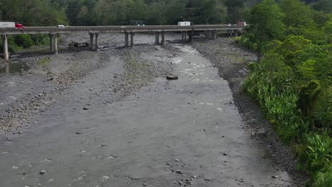 Commercial-vehicles-and-cars-crossing-bridge-over-river-affected-by-drought,-Aerial-dolly-in-shot