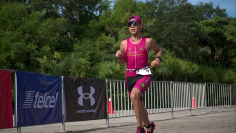 Cámara-Lenta-De-Un-Joven-Atleta-Con-Traje-Rosa-Y-Gafas-De-Sol-Corriendo-En-Una-Competencia-De-Triatlón-Que-Pasa