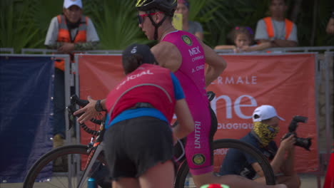 Competidor-Adolescente-Latino-Bajando-De-Su-Bicicleta-Descalzo-Mientras-Ingresa-A-La-Zona-De-Transición-En-Una-Competencia-De-Triatlón-Usando-Un-Traje-Rosa