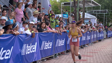 Sportlerin-Läuft-Joggen-Bei-Einem-Triathlon-Wettkampf-Neben-Den-Zuschauern,-Die-Sie-Anfeuern