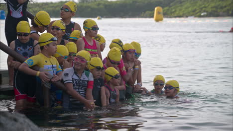 Grupo-De-Jóvenes-Niños-Latinos-Concursantes-Participantes-Competidores-Esperando-Que-Comience-La-Competencia-De-Triatlón-Listos-Para-Entrar-Al-Agua